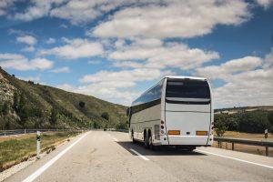 A white coach, or long haul bus for tourists drives through the open roads of Spain, Europe on a summer day. There are white clouds against a blue sky and countryside.